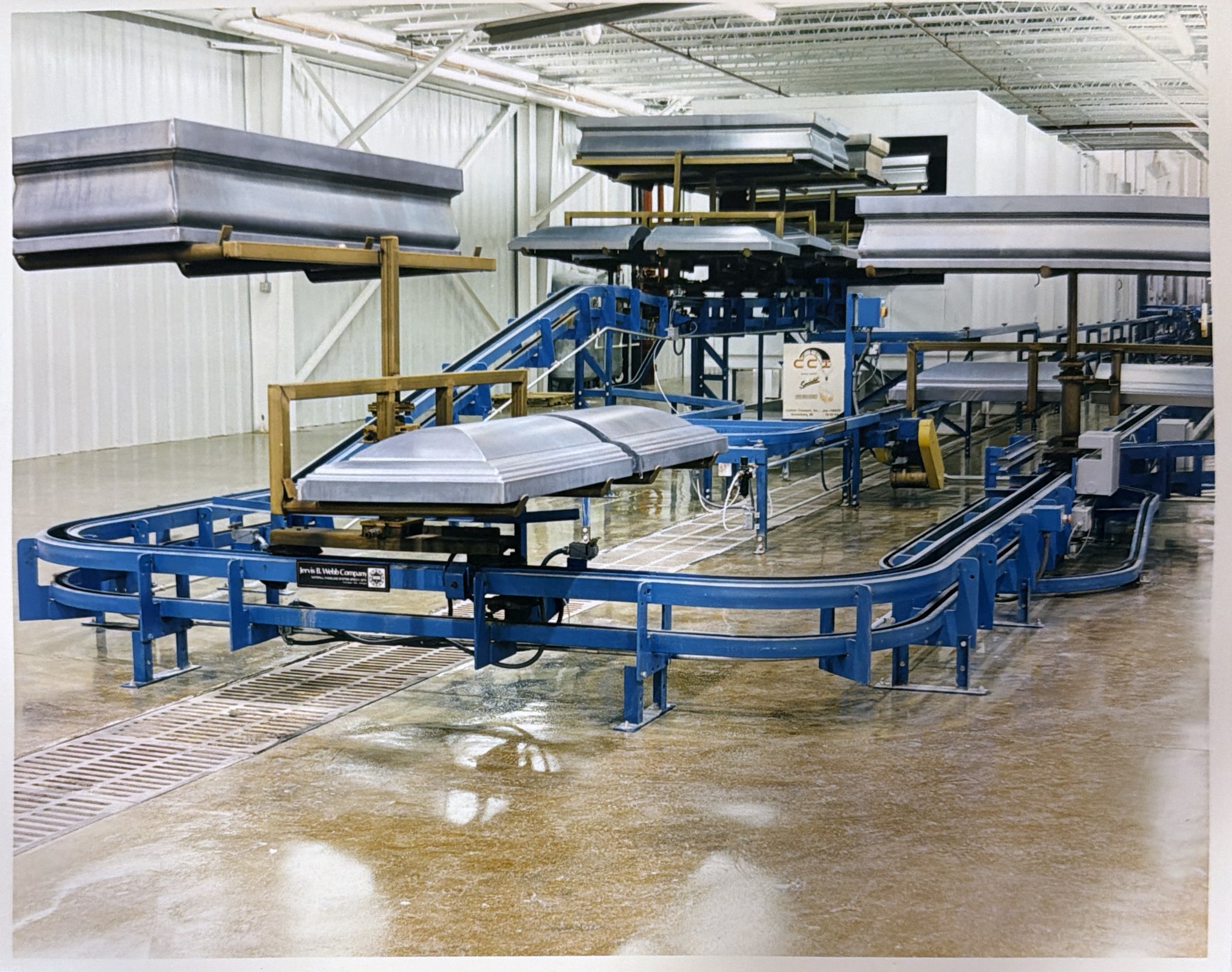 Curved blue inverted conveyor track carrying elevated metal components in Aurora, Indiana.
