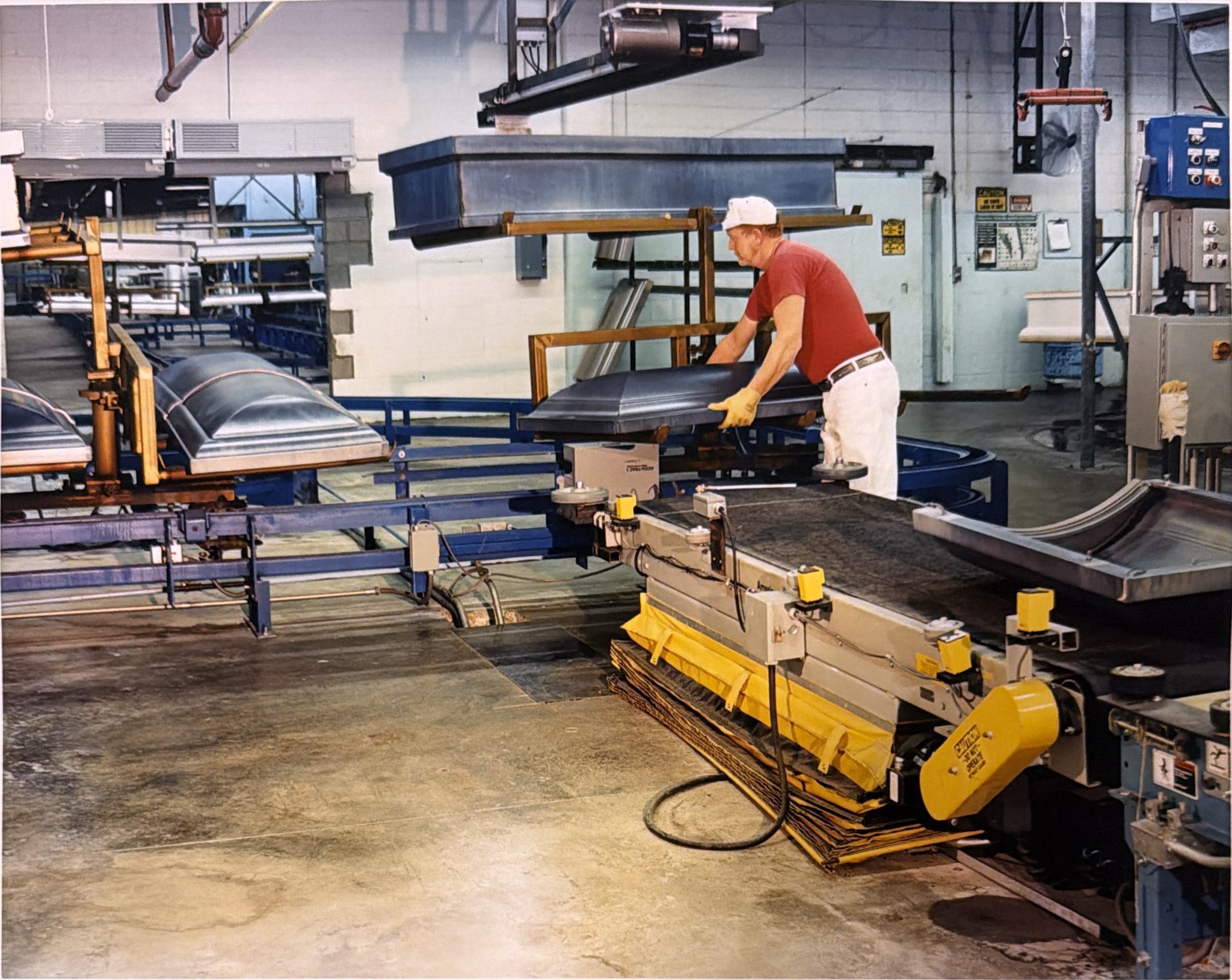 An operator handling a component beside the inverted conveyor and adjacent workstation.