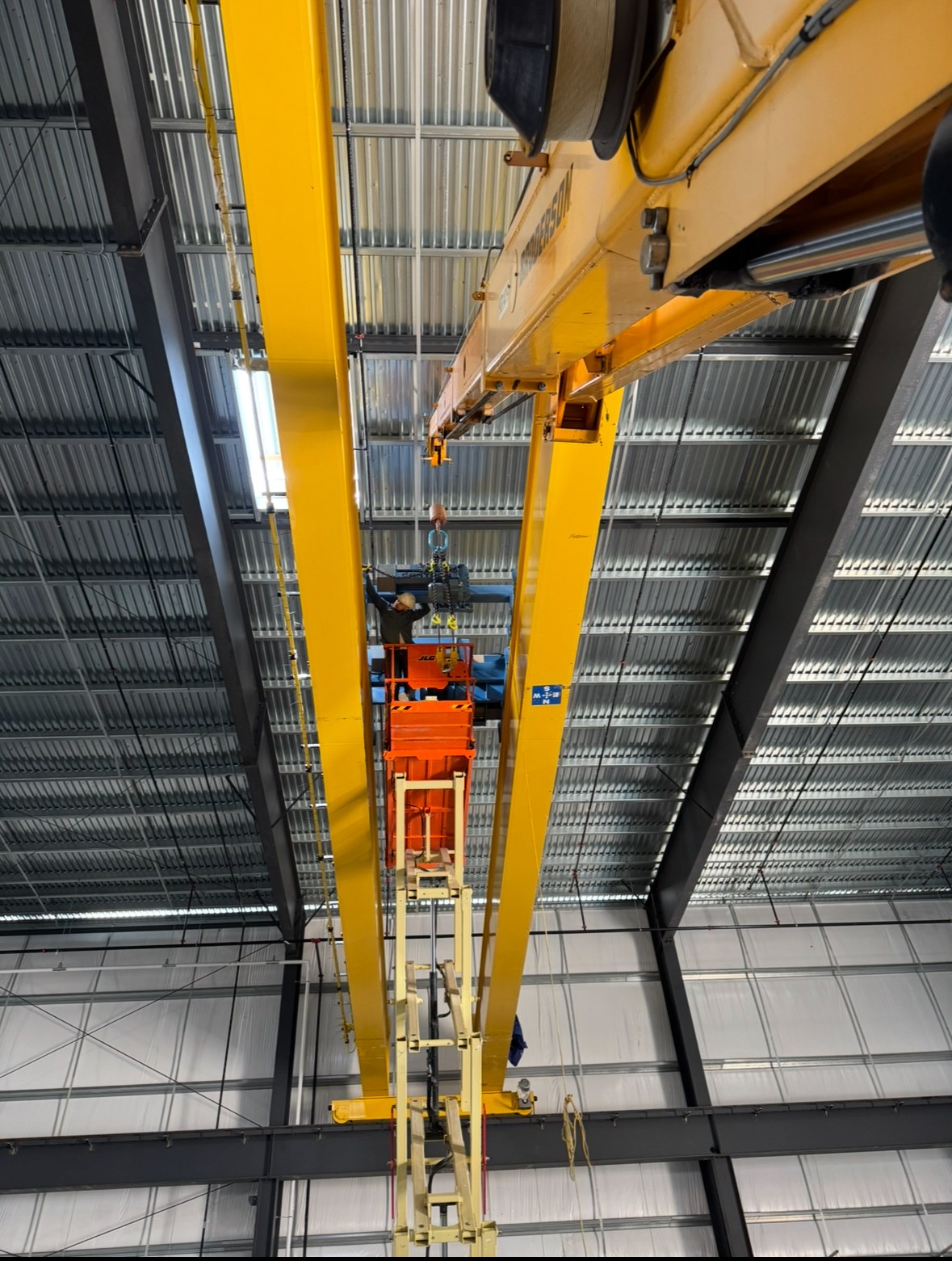 Hoist installation work between the girders using a mobile crane and elevated platform.