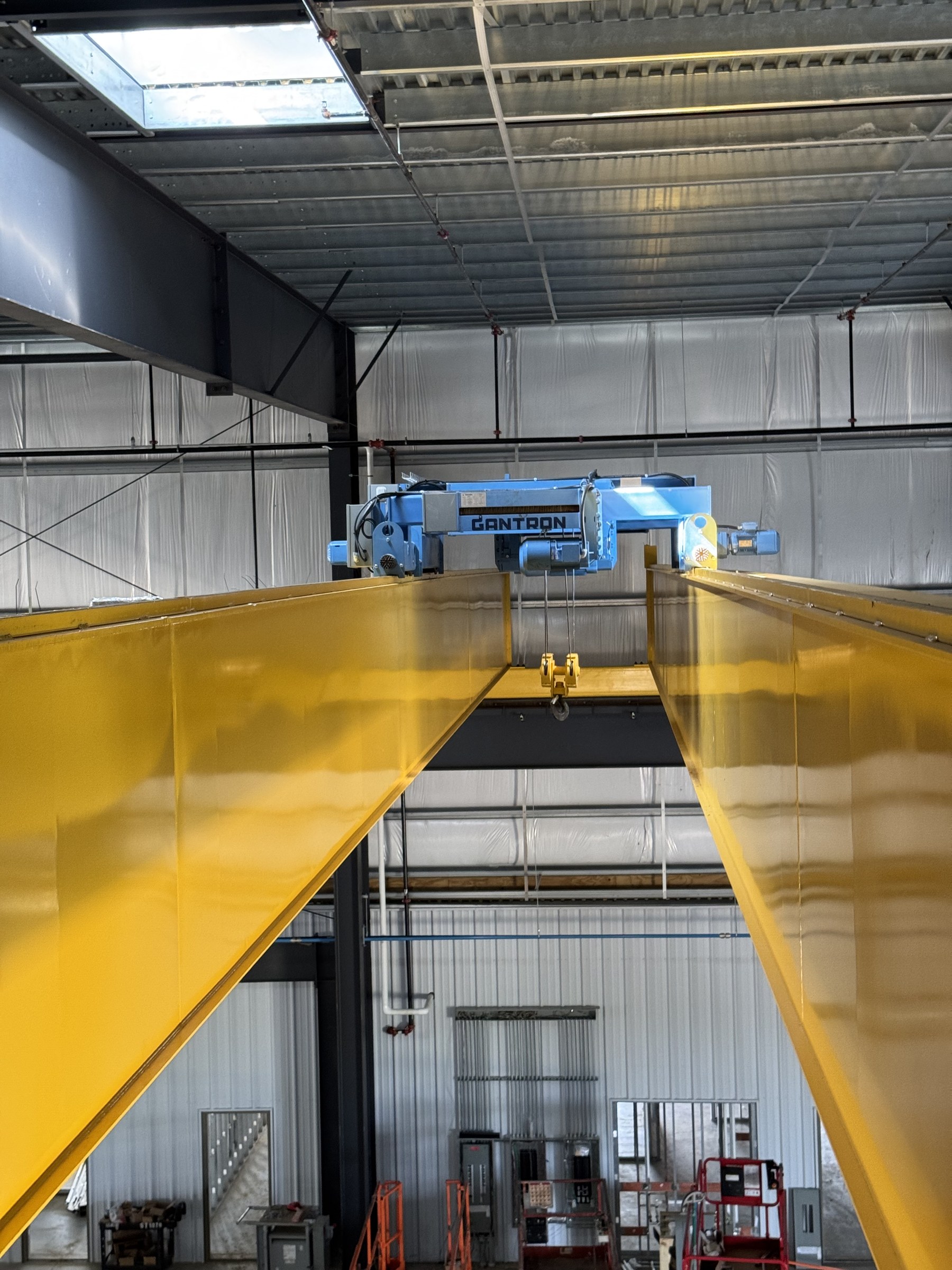 Blue hoist equipment and a suspended hook between the yellow bridge girders.