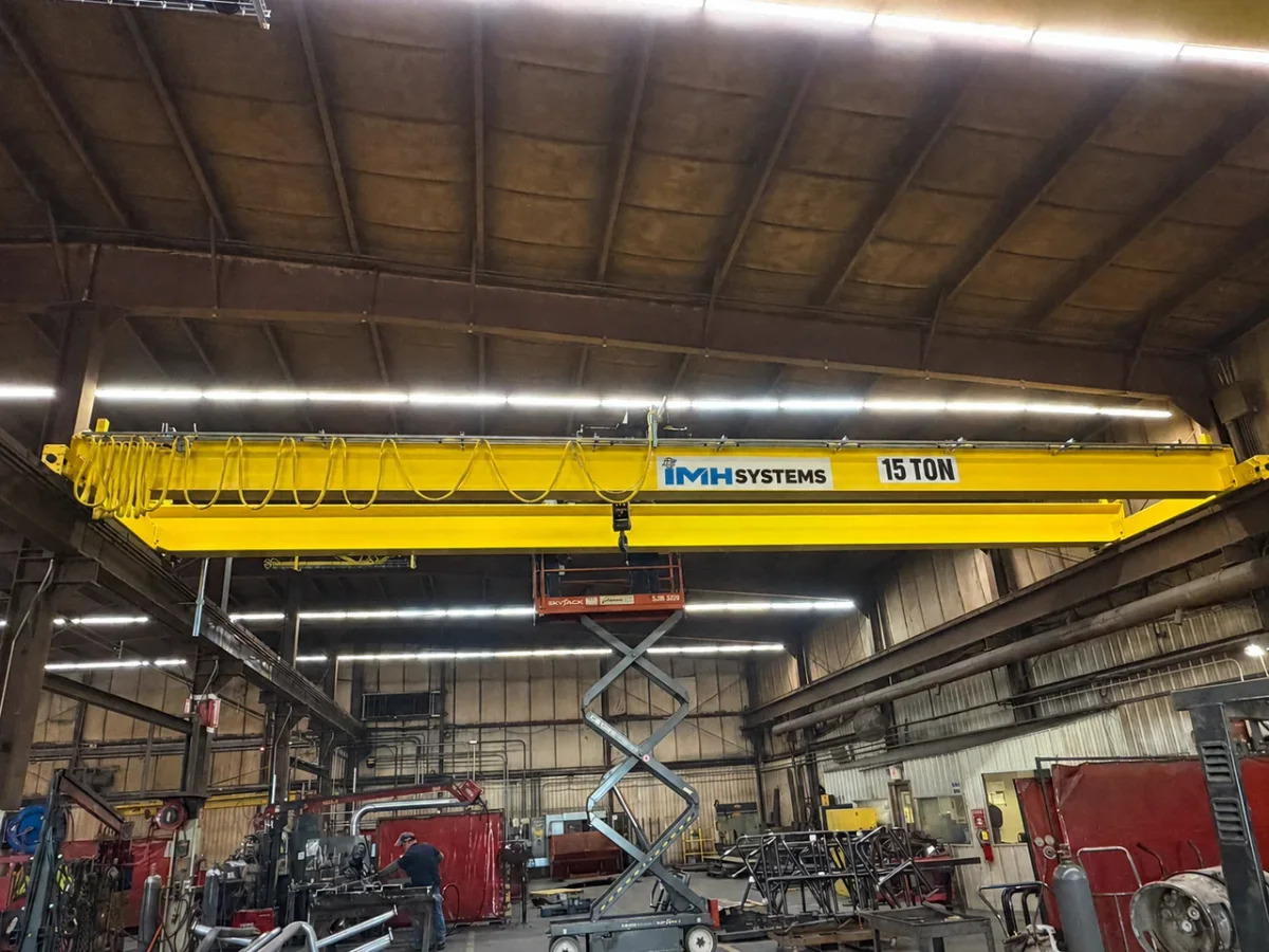Yellow IMH Systems bridge crane marked 15 ton spanning a fabrication bay with an access lift below.