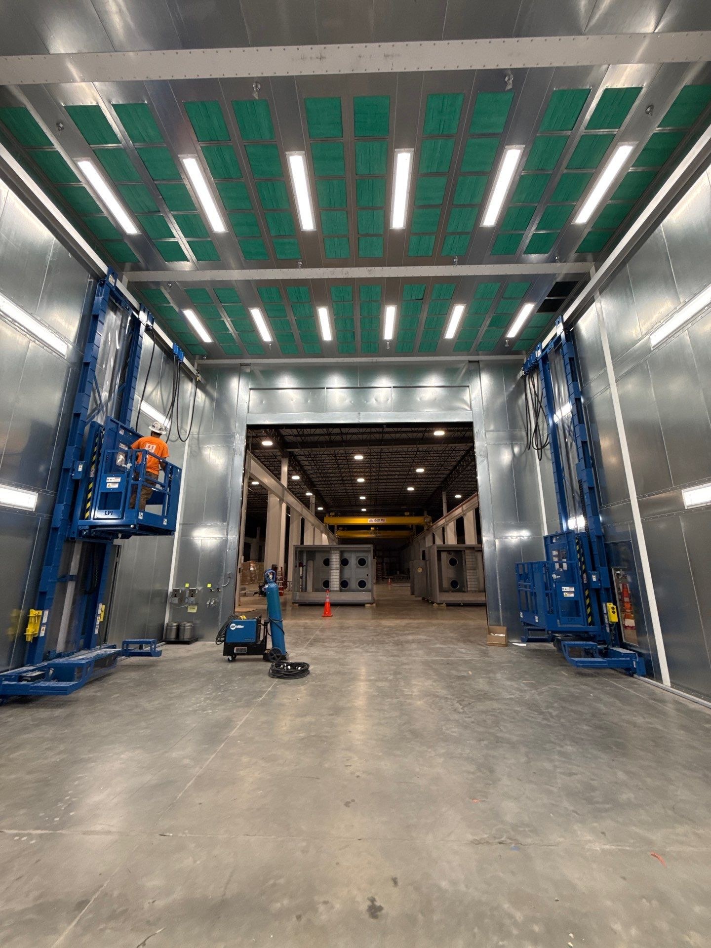 Installed man lifts on both sides of the illuminated spray booth.