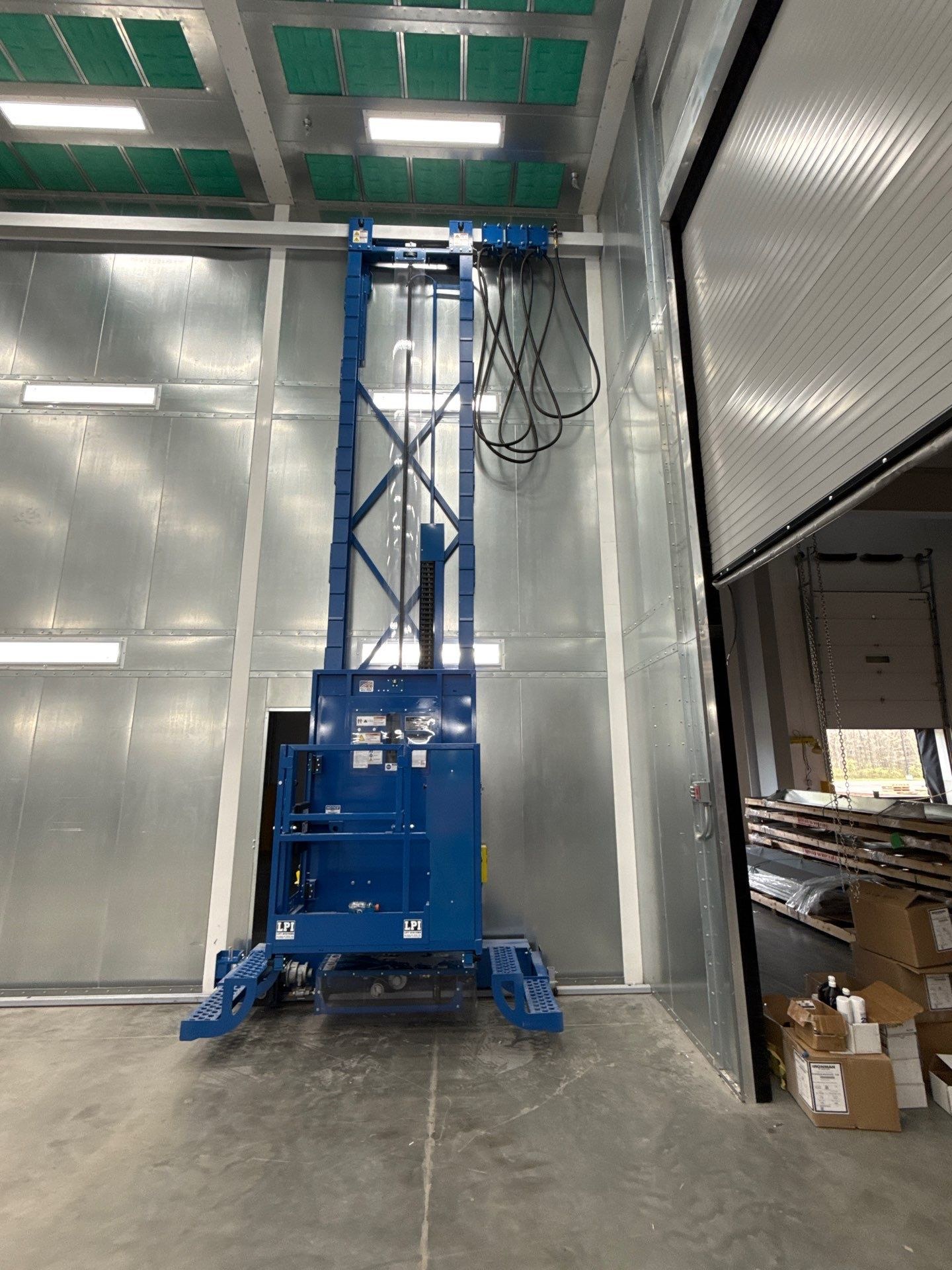 Installed blue man lift, showing the platform, vertical mast, and overhead hose routing.