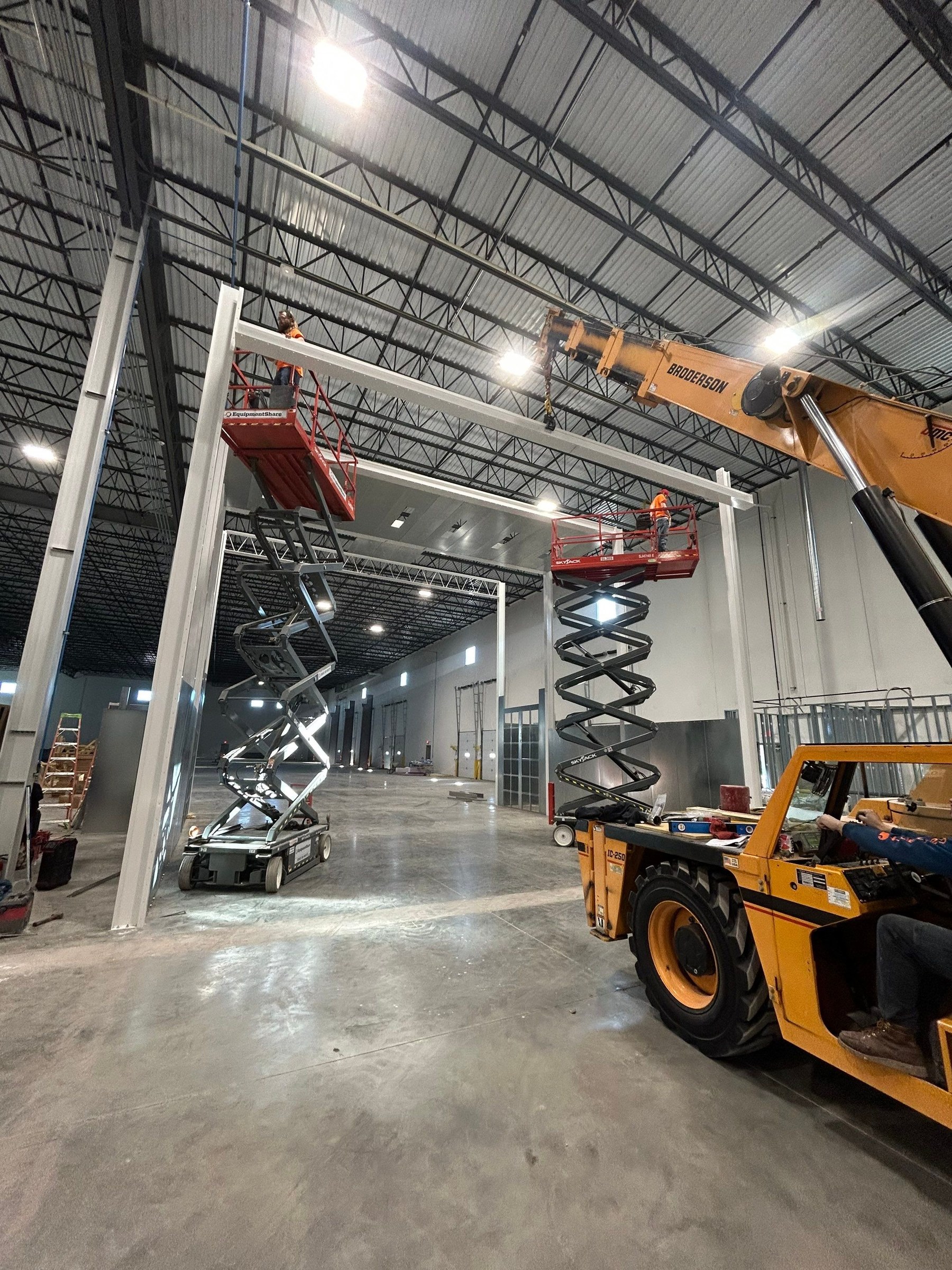 Installers on scissor lifts positioning an overhead member with a mobile crane.