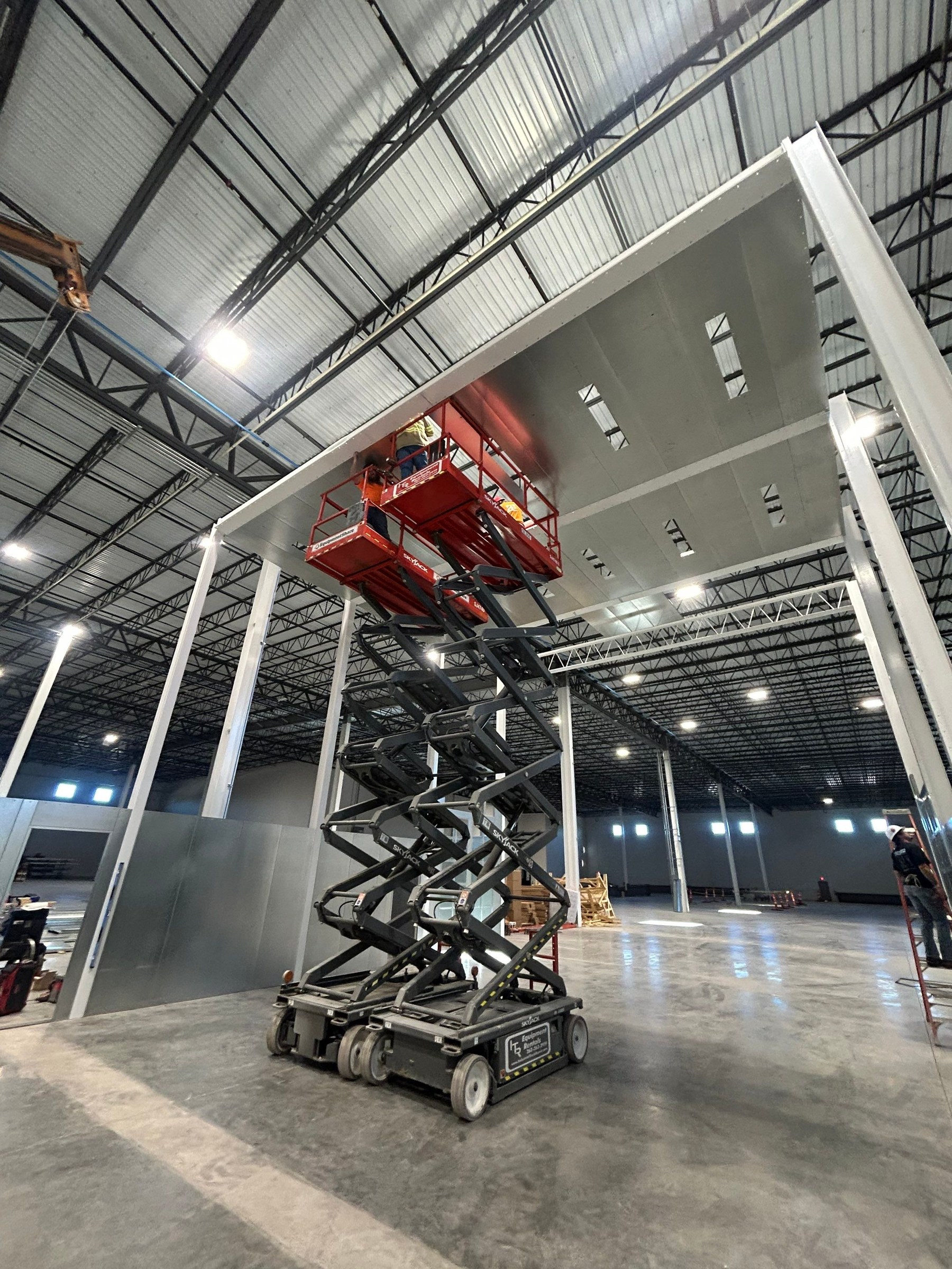 Crews working from scissor lifts beneath the booth ceiling panels.