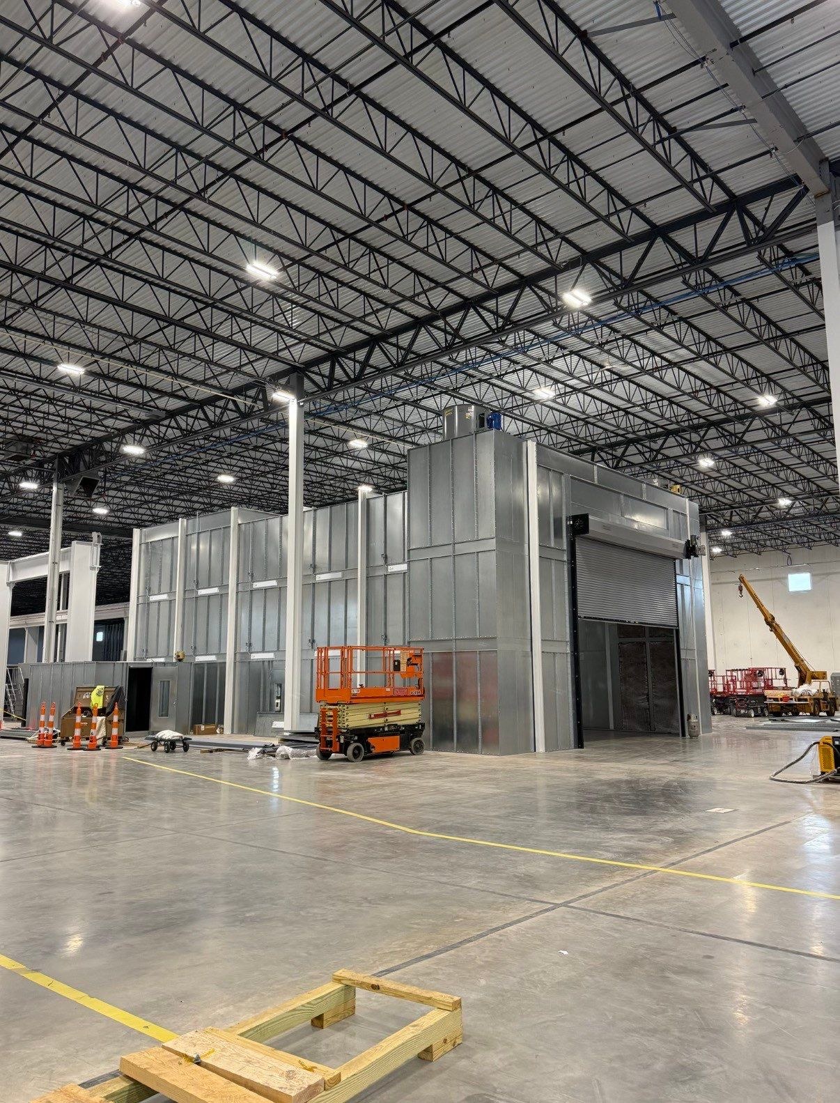Spray booth exterior with a partially open roll-up door and adjacent mix-room enclosure.