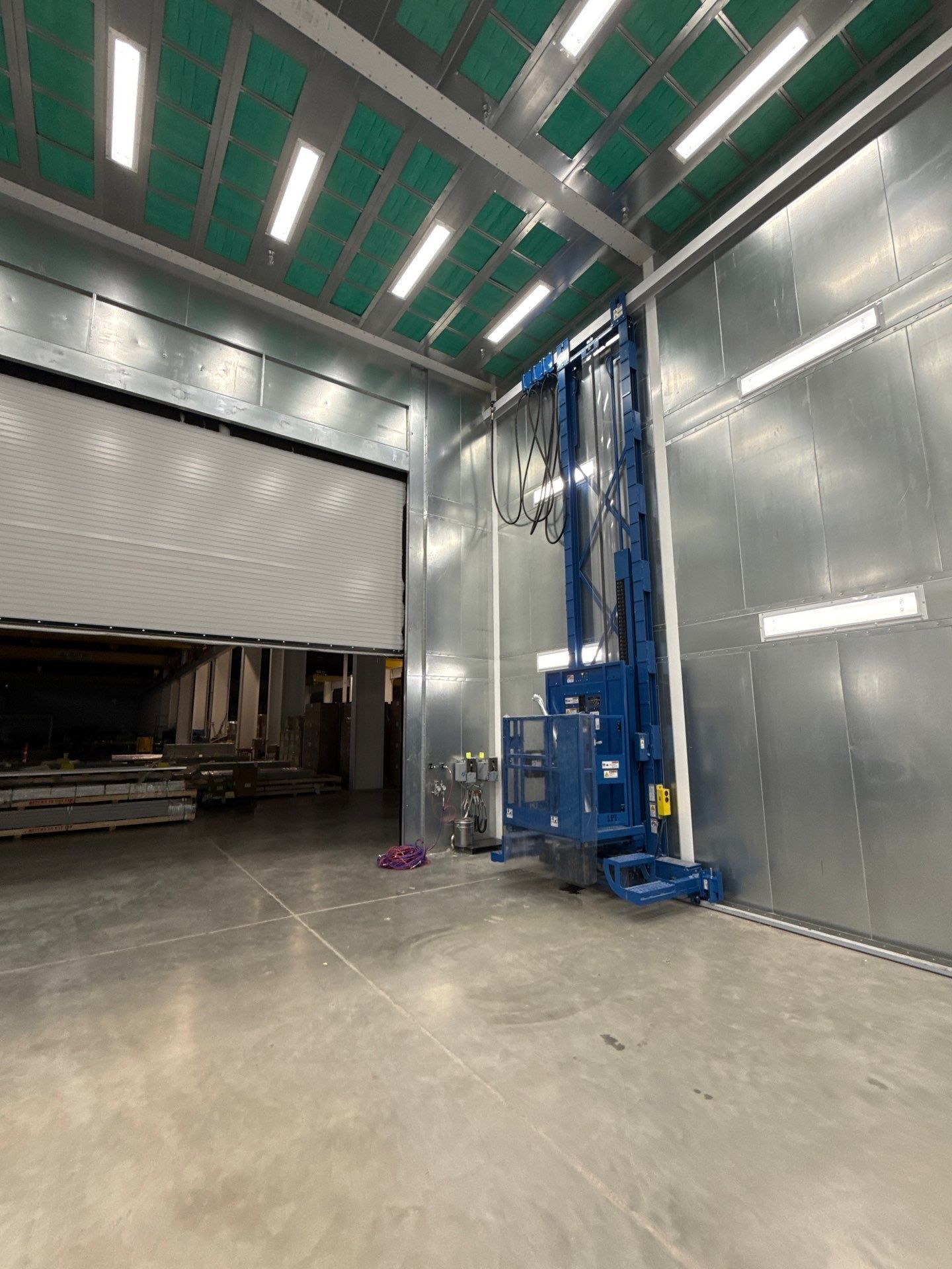 Installed man lift on the right side of the booth entrance beneath the ceiling filters and lights.