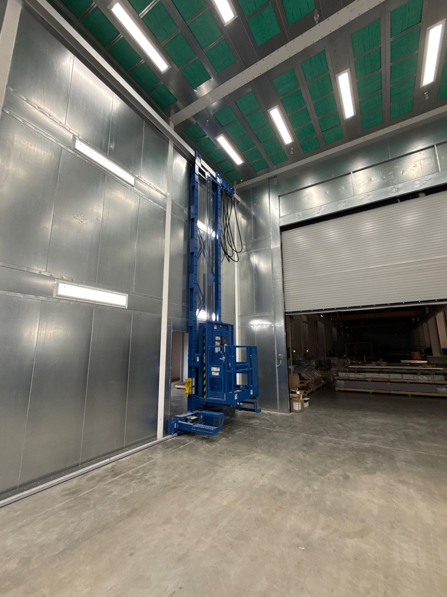 Installed man lift on the left side of the booth entrance, with the platform and mast visible.
