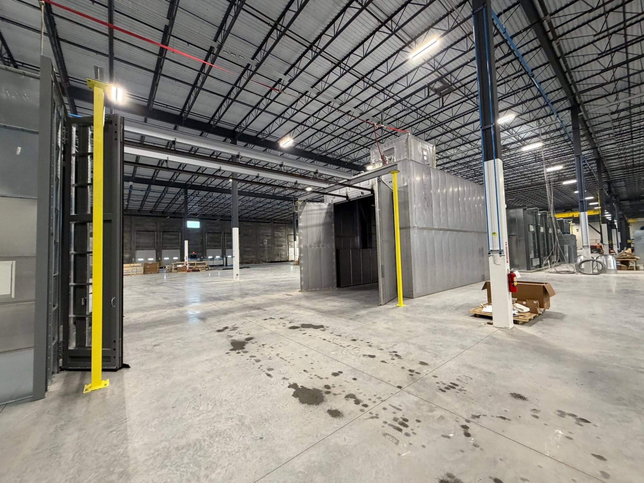Overhead conveyor rails and yellow support columns beside a large coating-process opening.