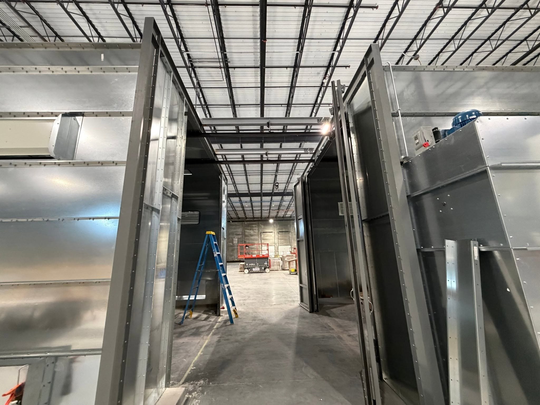 Conveyor rails crossing the space between two process enclosures during installation.