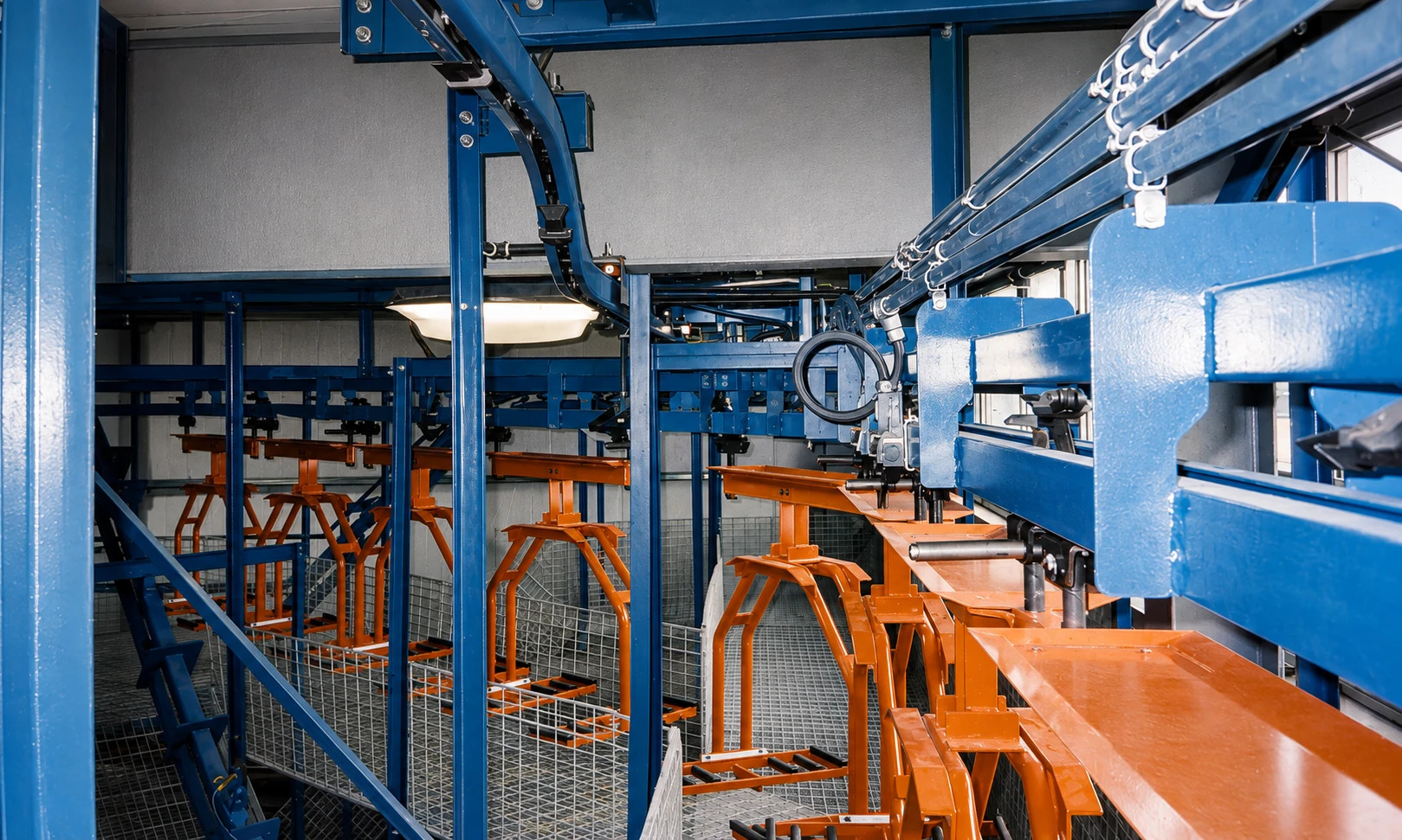 Close view of blue conveyor track, carrier mechanisms, support steel, and orange suspended fixtures.