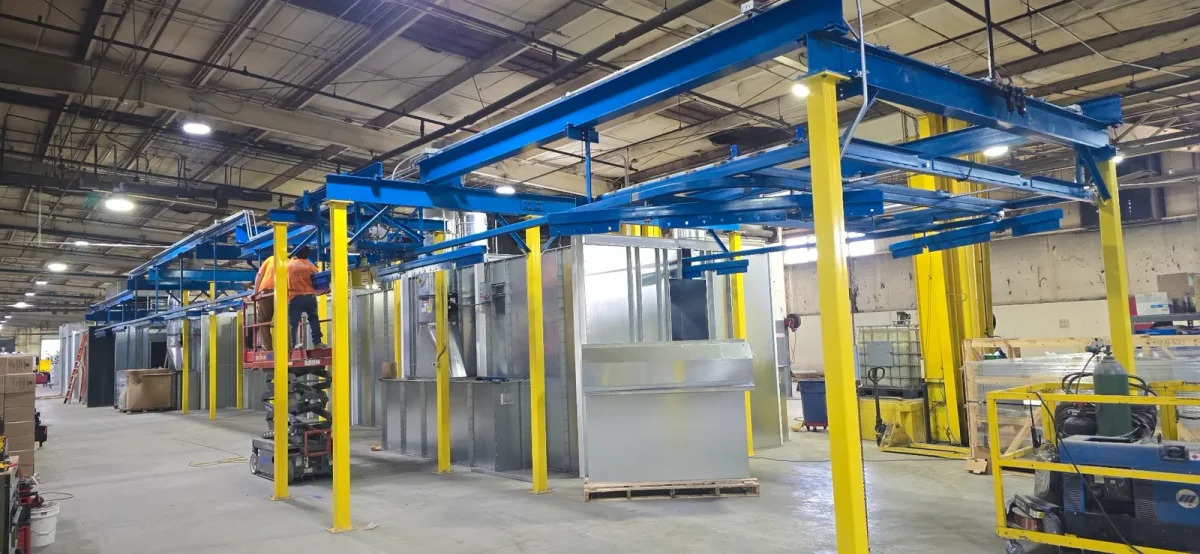 Installers on a scissor lift beside blue overhead conveyor track and yellow support columns.