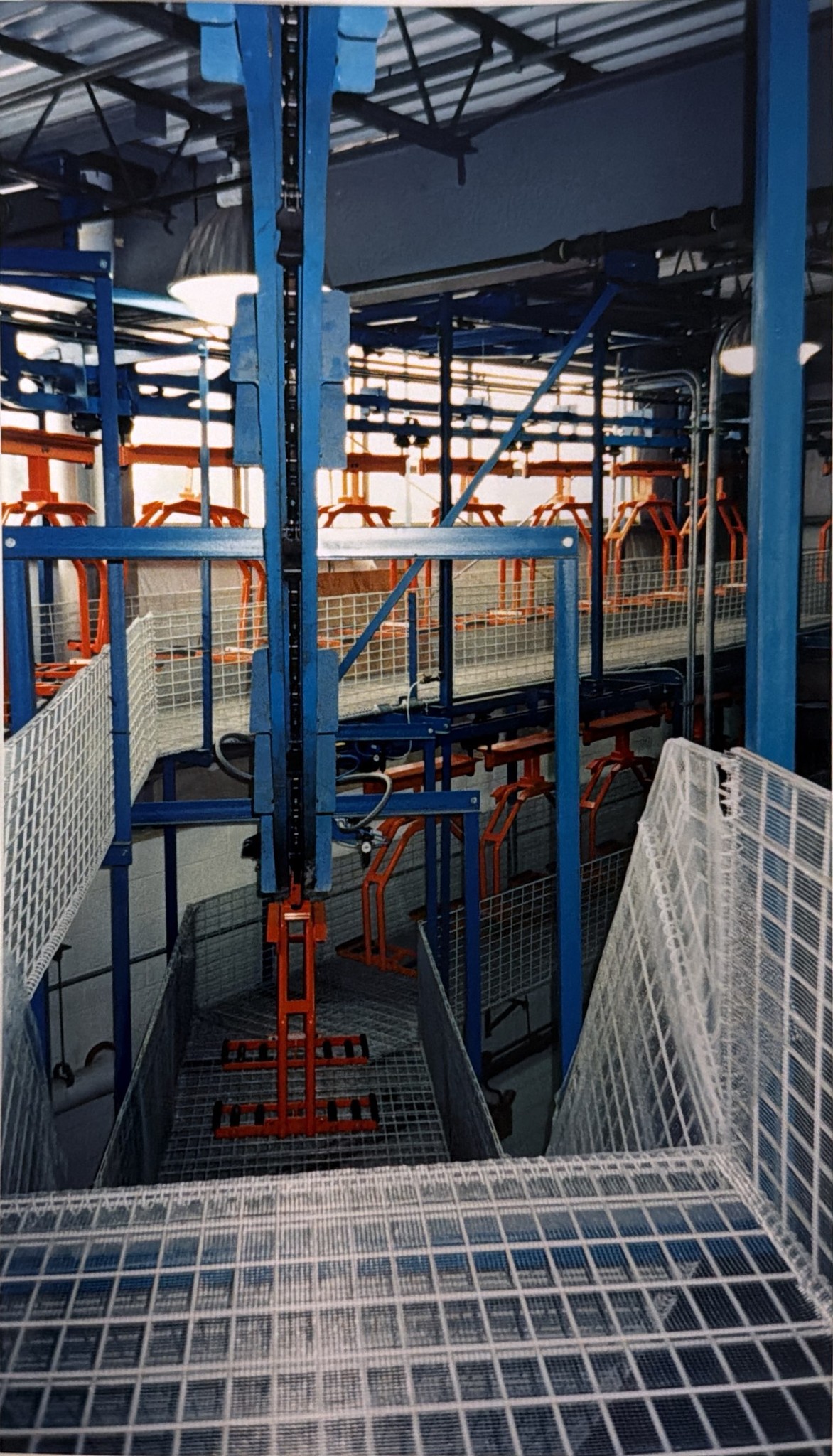 Orange carriers, blue support steel, and white guarding along the conveyor route.