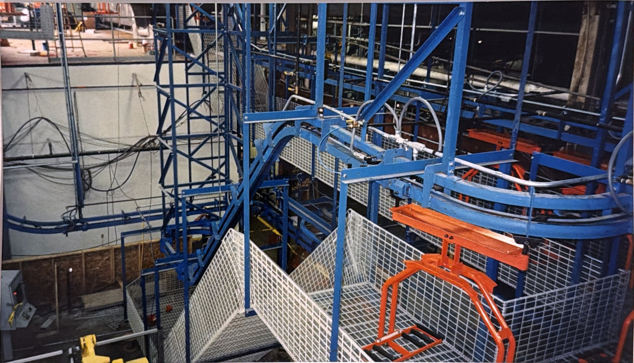 Blue power-and-free track changing elevation beside the supporting frame and guarded work area.