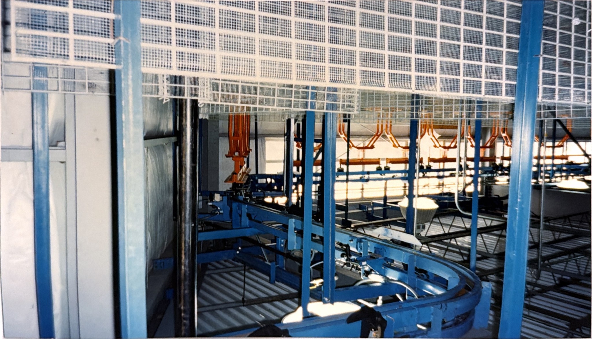 Curved blue conveyor track and orange carriers beneath white mesh guarding.