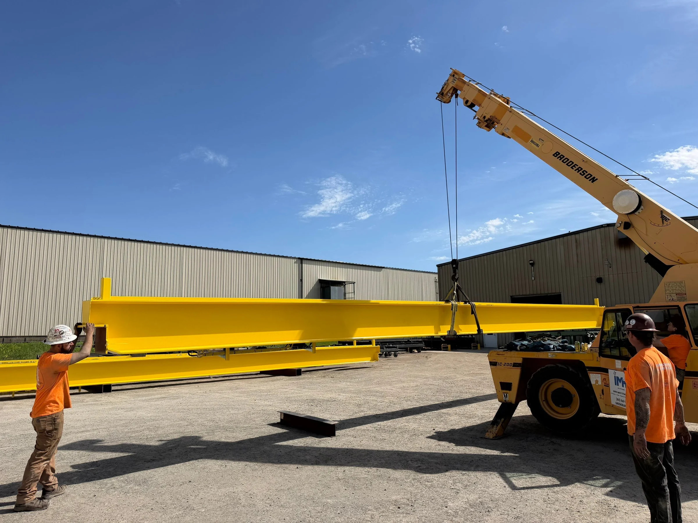 IMH crew and mobile crane handling a new yellow bridge girder in the yard