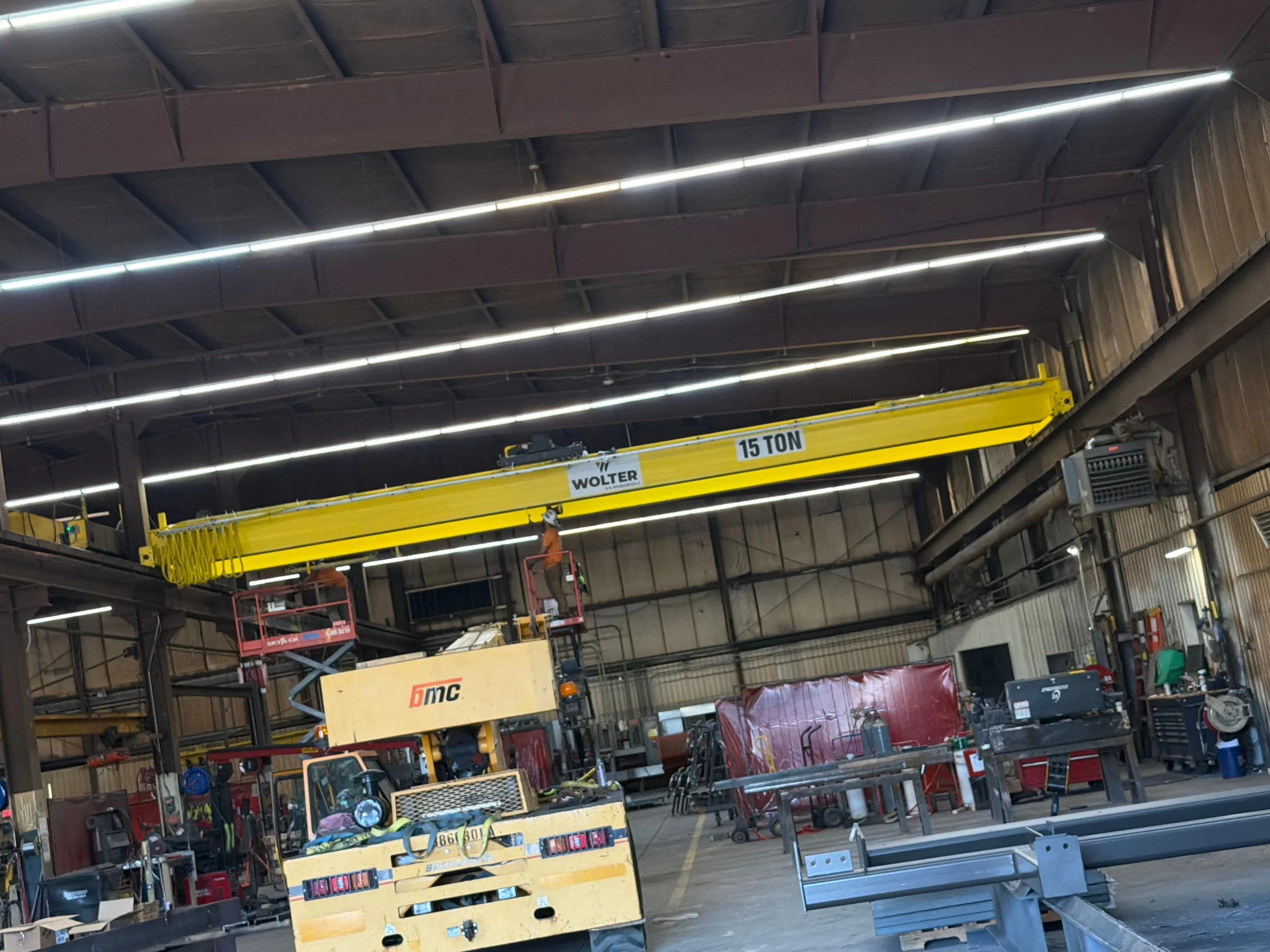 New Wolter 15-ton bridge crane at runway height with installers on access lifts and a mobile crane below