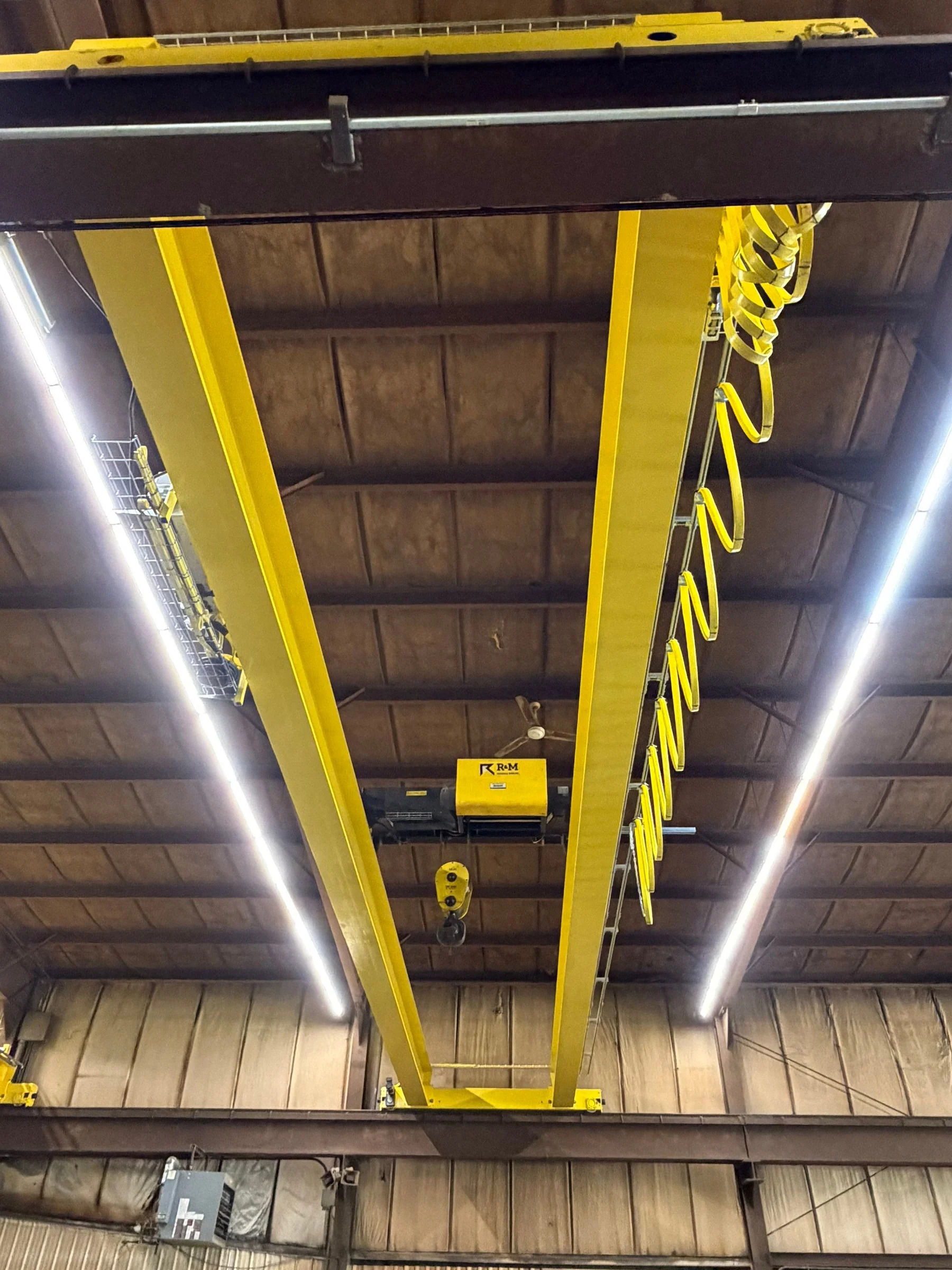 New double-girder bridge crane viewed from below, showing the hoist and yellow festoon cables