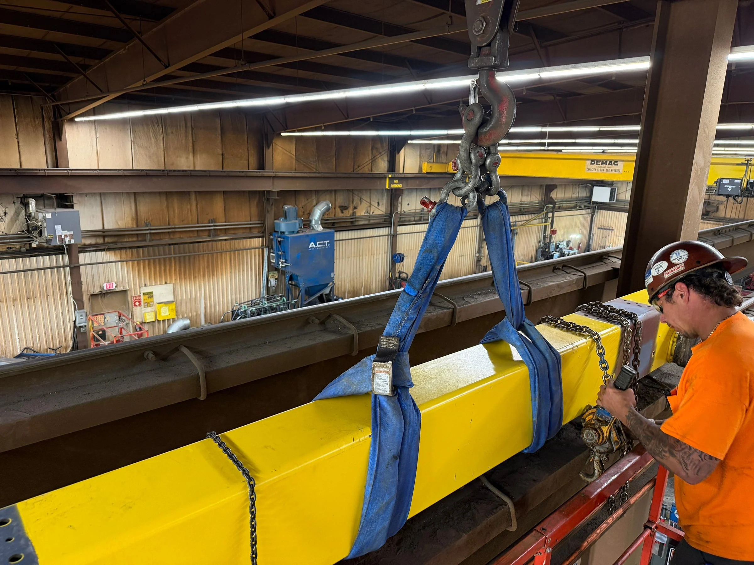 Installer beside an old yellow bridge girder with blue lifting slings and chain rigging