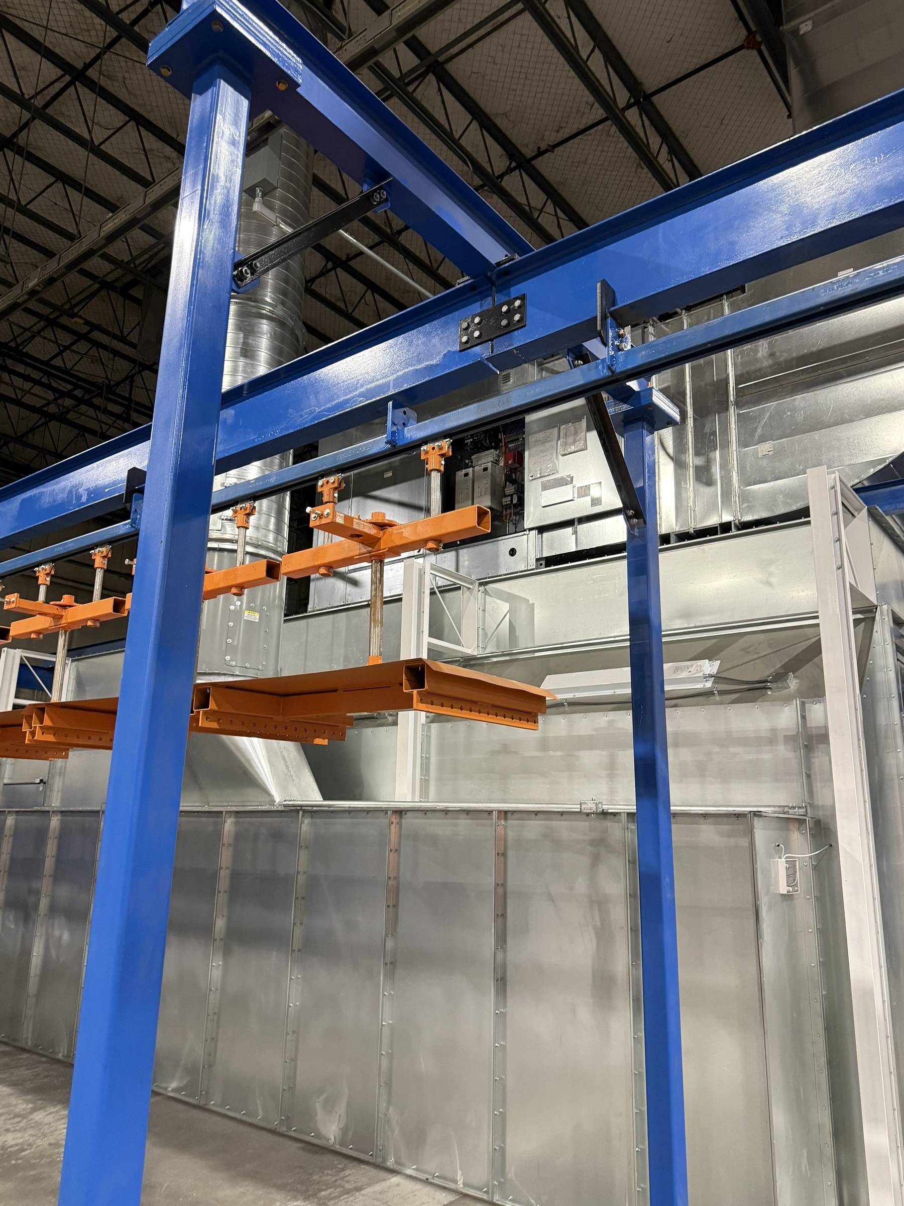 Custom orange carriers suspended beneath the overhead track and bolted blue support frame.
