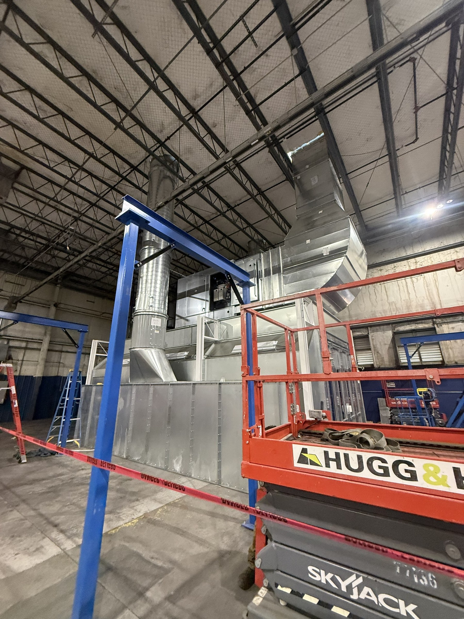 Work from a scissor lift around the blue support frame and booth enclosure.