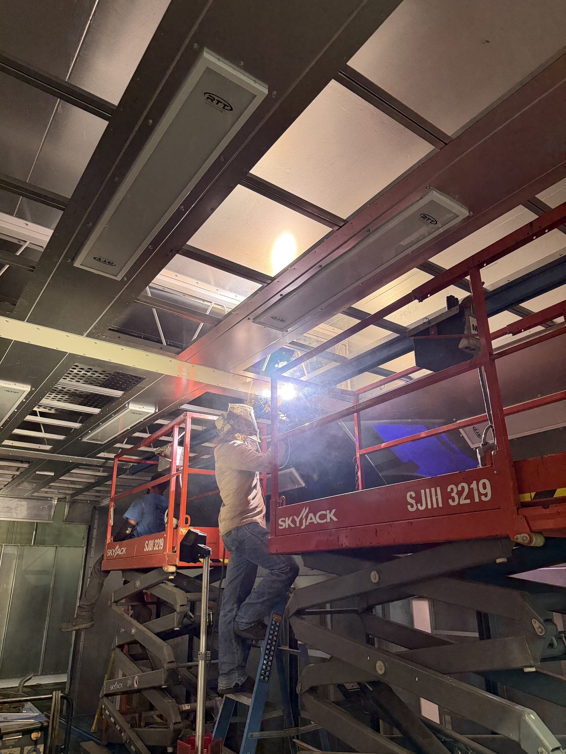Installation work beneath the overhead route and booth ceiling.