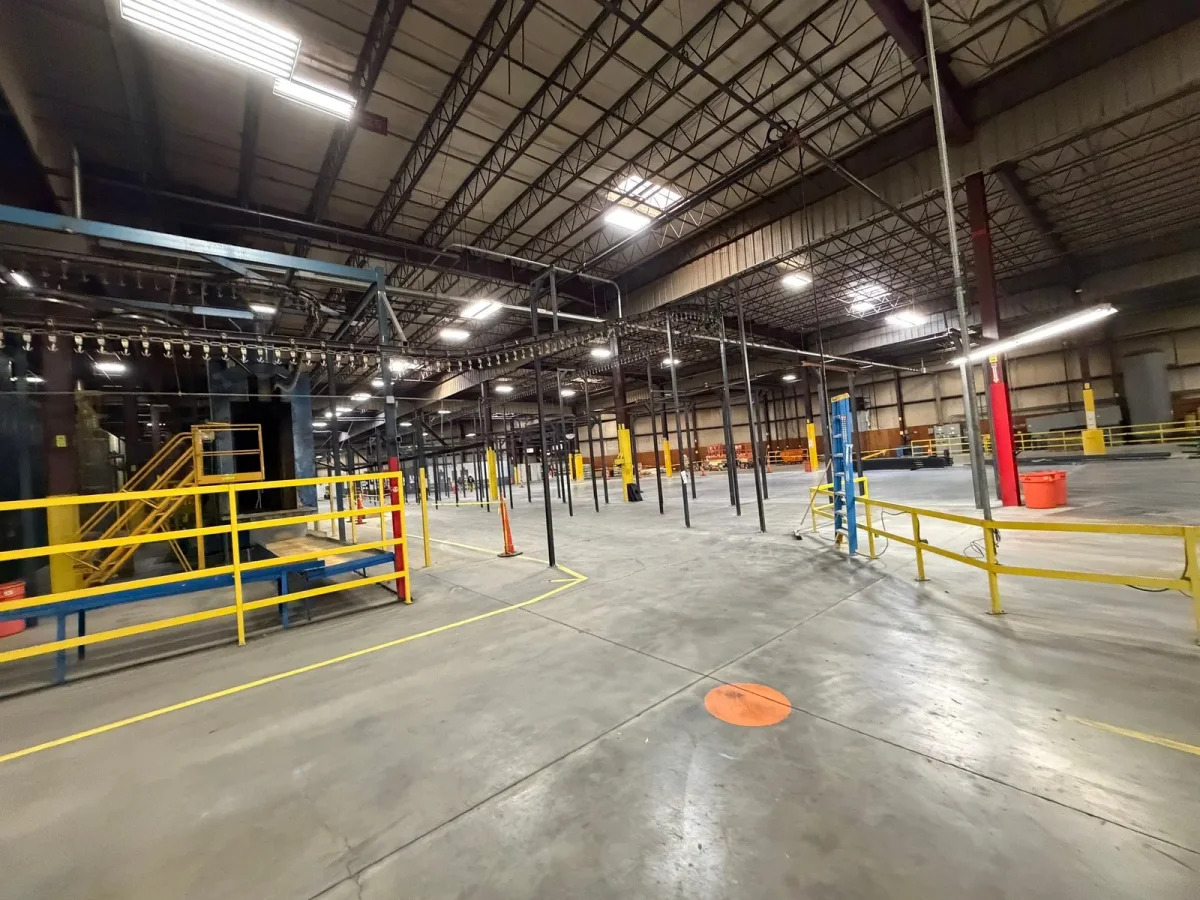 Wide production bay with overhead monorail routing, support columns, and yellow guardrails.