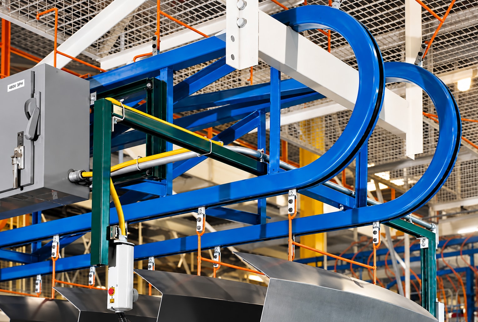 Close view of curved blue Over-N-Under tracks, orange carriers, and suspended metal parts.