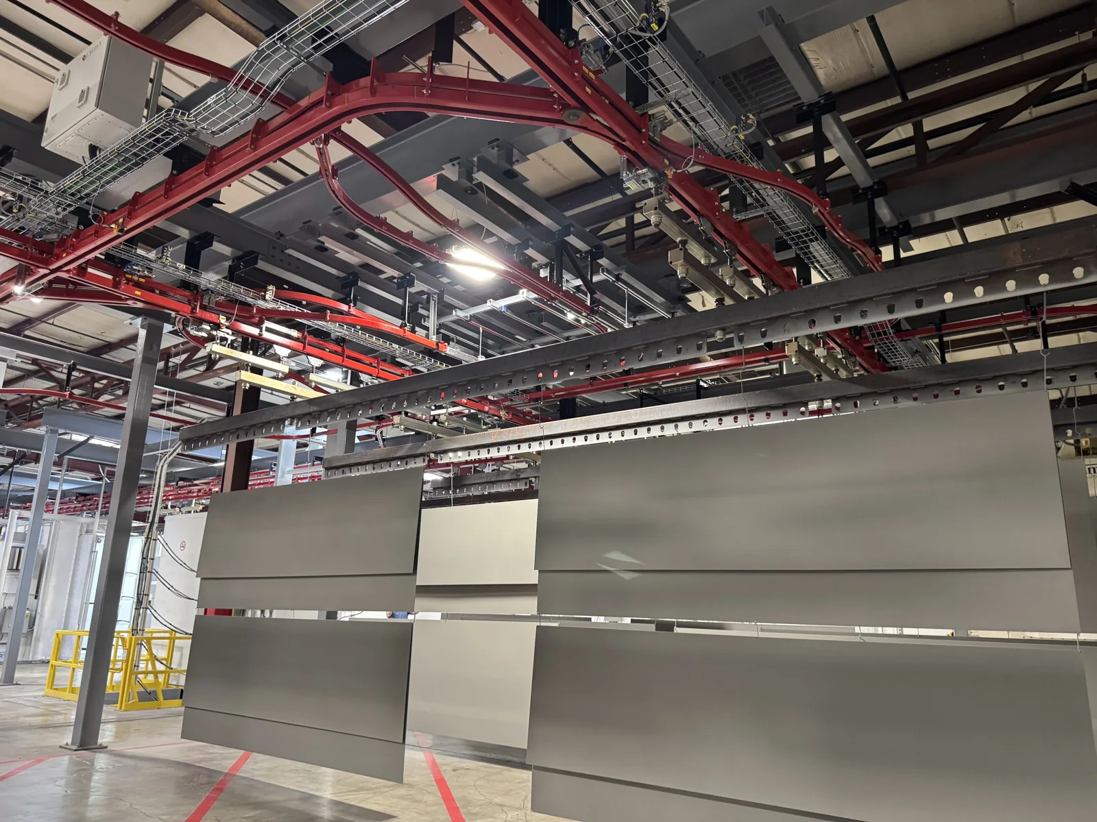 Red overhead power-and-free track and carriers with metal panels suspended through a finishing area.