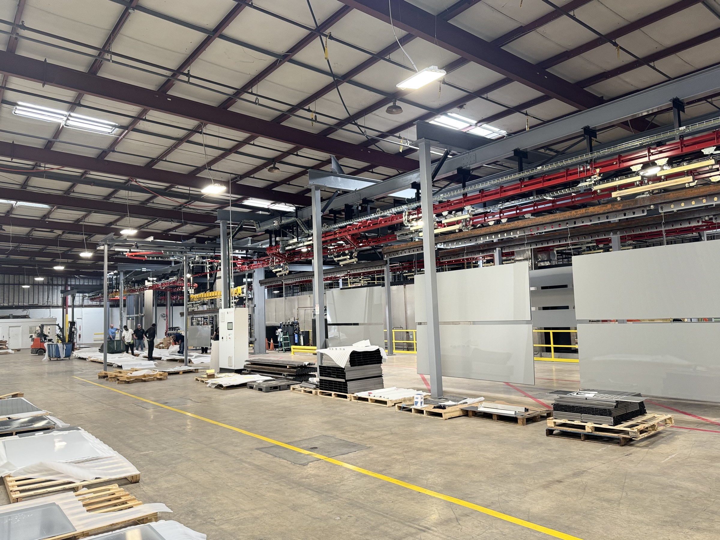 Overall installation view with red power-and-free track, gray support steel, and suspended panels.