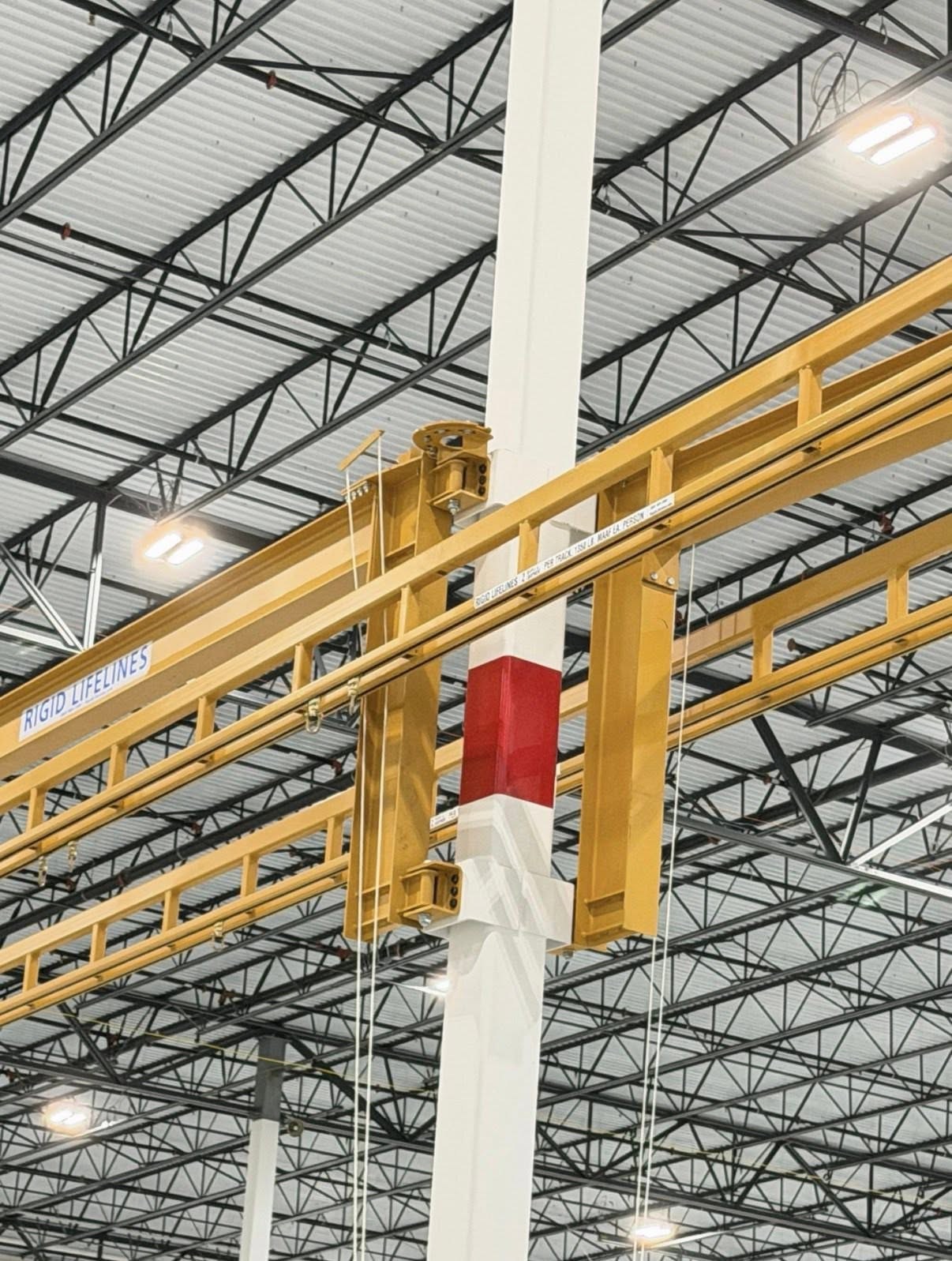 Close view of the yellow rigid-lifeline rails and their support connection at a building column.