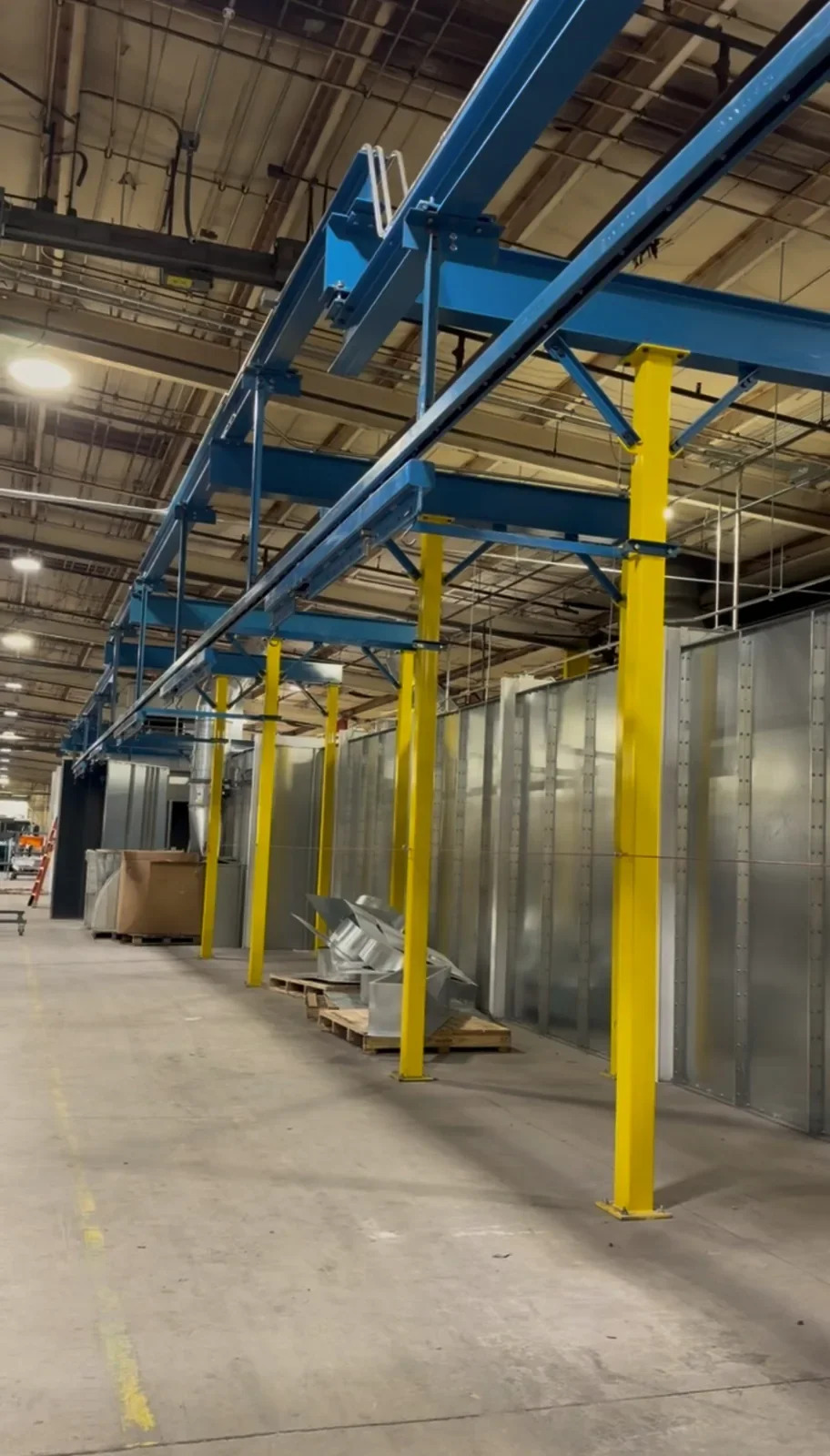 Close view along blue overhead conveyor rail, suspension brackets, supporting beams, and yellow columns.