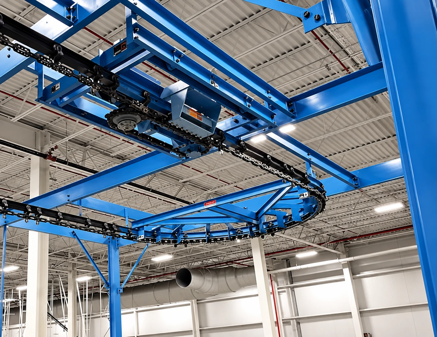 Overhead view from below of an I-beam conveyor drive, curved chain route, and bolted blue support steel