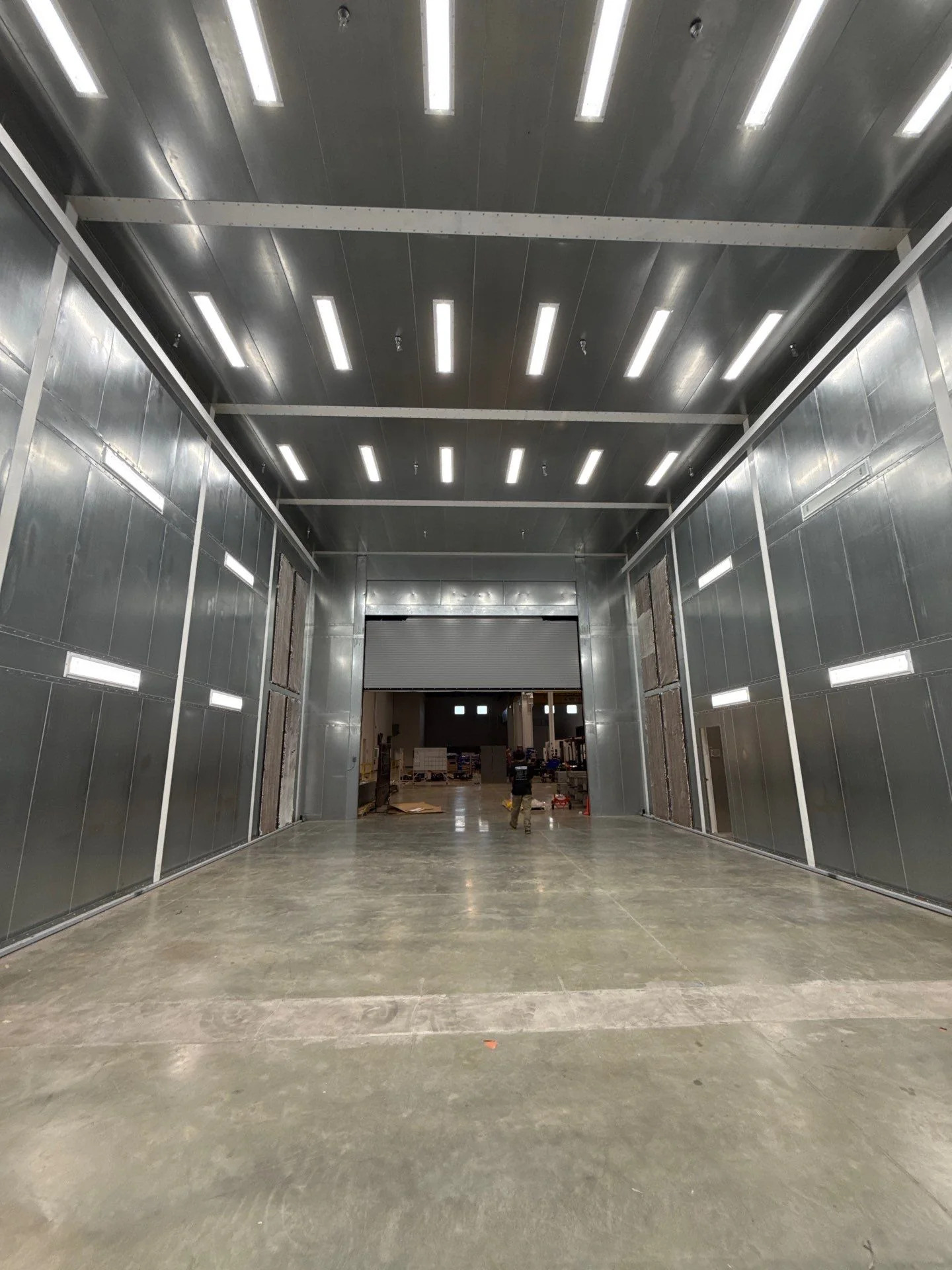 Large industrial booth interior with precisely assembled metal panels, overhead lighting, and a full-height access opening