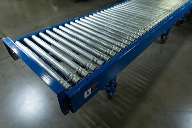 Metal rollers mounted in a blue conveyor frame with floor supports.