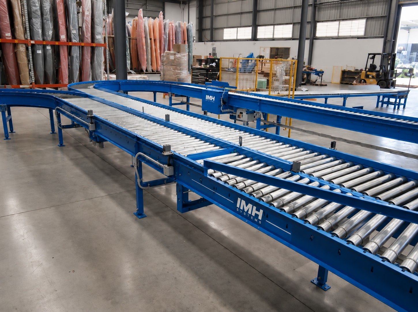 IMH-branded blue roller conveyor system with straight and curved sections inside a facility.